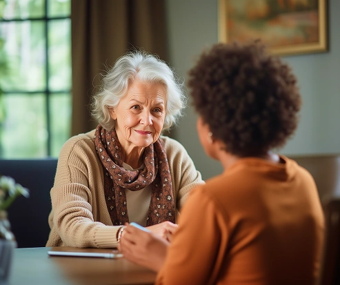 Smiling senior woman talking with another woman at a table in a cozy, well-lit room
