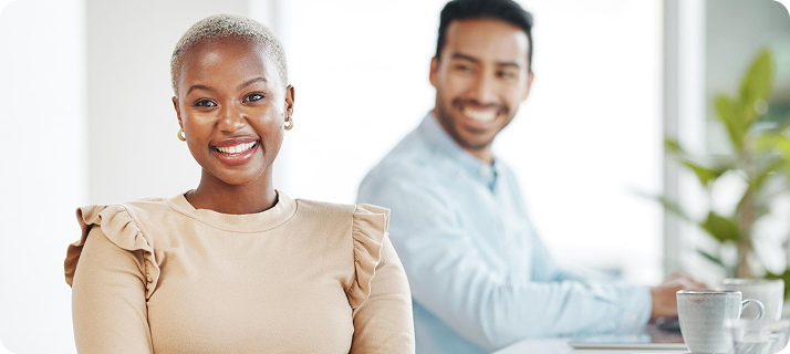 Smiling woman and man in an office setting, engaged in conversation and appearing friendly and professional.