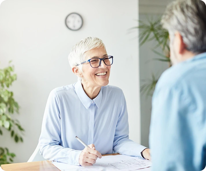 A woman with short gray hair and glasses smiles while sitting at a des