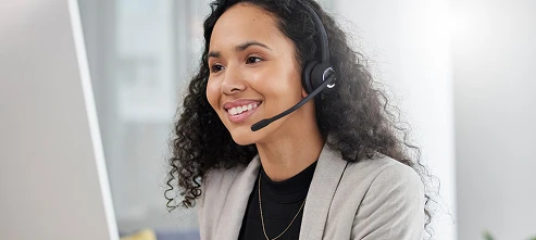 Smiling woman with curly hair wearing a headset and blazer, working at a computer