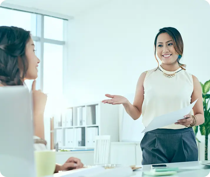 Woman presenting a document while speaking to a colleague in an office.